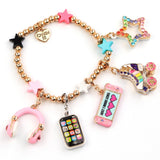A gold-tone bead charm bracelet featuring various pop culture and fashion-themed charms, including a pink heart-shaped star, a rainbow star, a roller skate charm, a pink headphone charm, a phone charm, and a heart-shaped charm